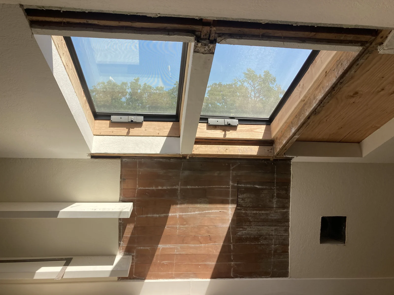 Skylight surround before drywall repair — exposed wood beams, raw plaster, and unfinished framing visible around the skylights